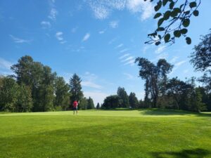 A golfer lines up a putt under a bright summer sky — wide fairways and natural beauty define the Burnaby Mountain experience.