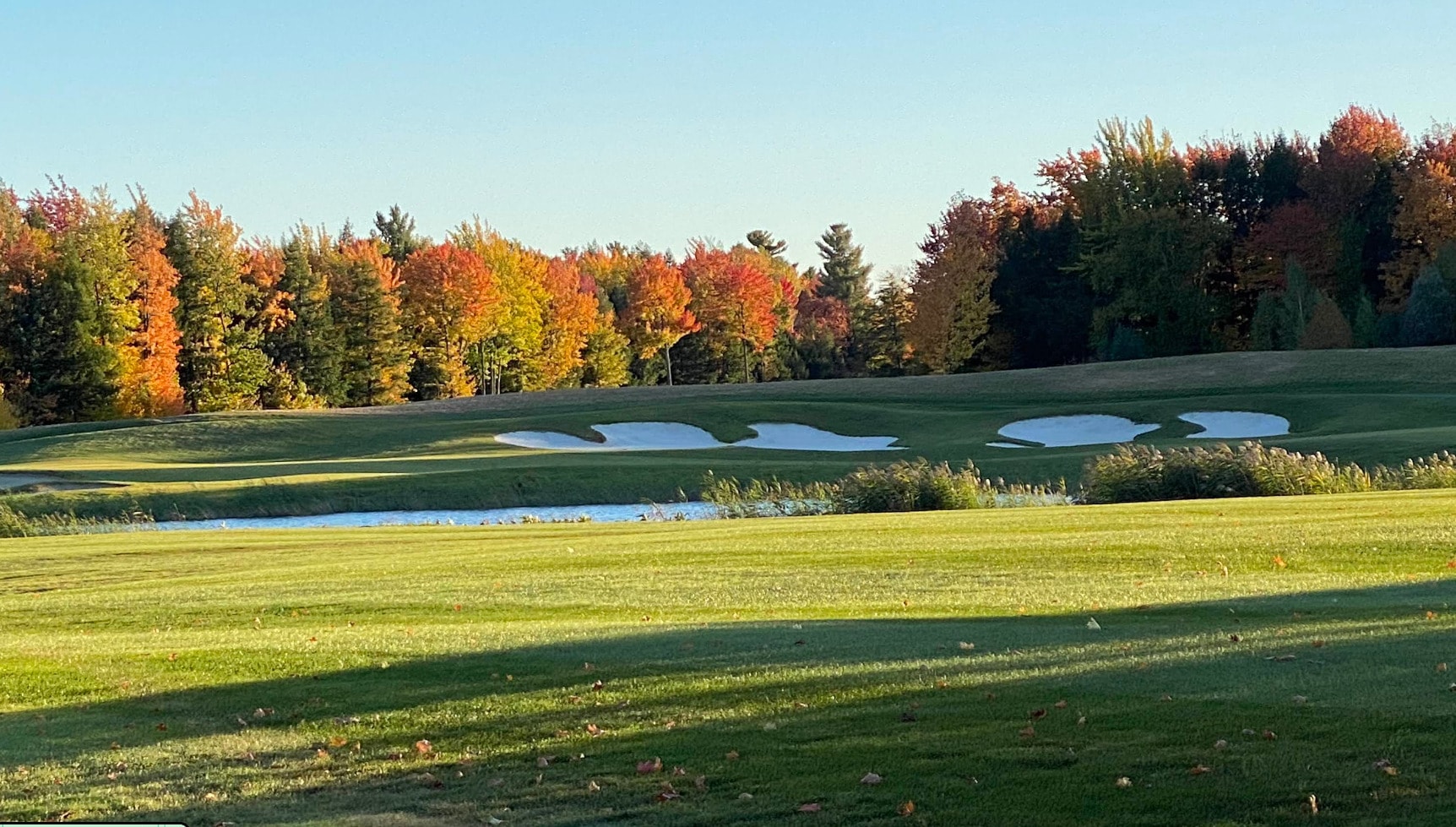 A scenic autumn view at Golf Le Fontainebleau, where colorful fall trees frame the fairway and bright white bunkers add striking contrast under the cl A scenic autumn view at Golf Le Fontainebleau, where colorful fall trees frame the fairway and bright white bunkers add striking contrast under the cl