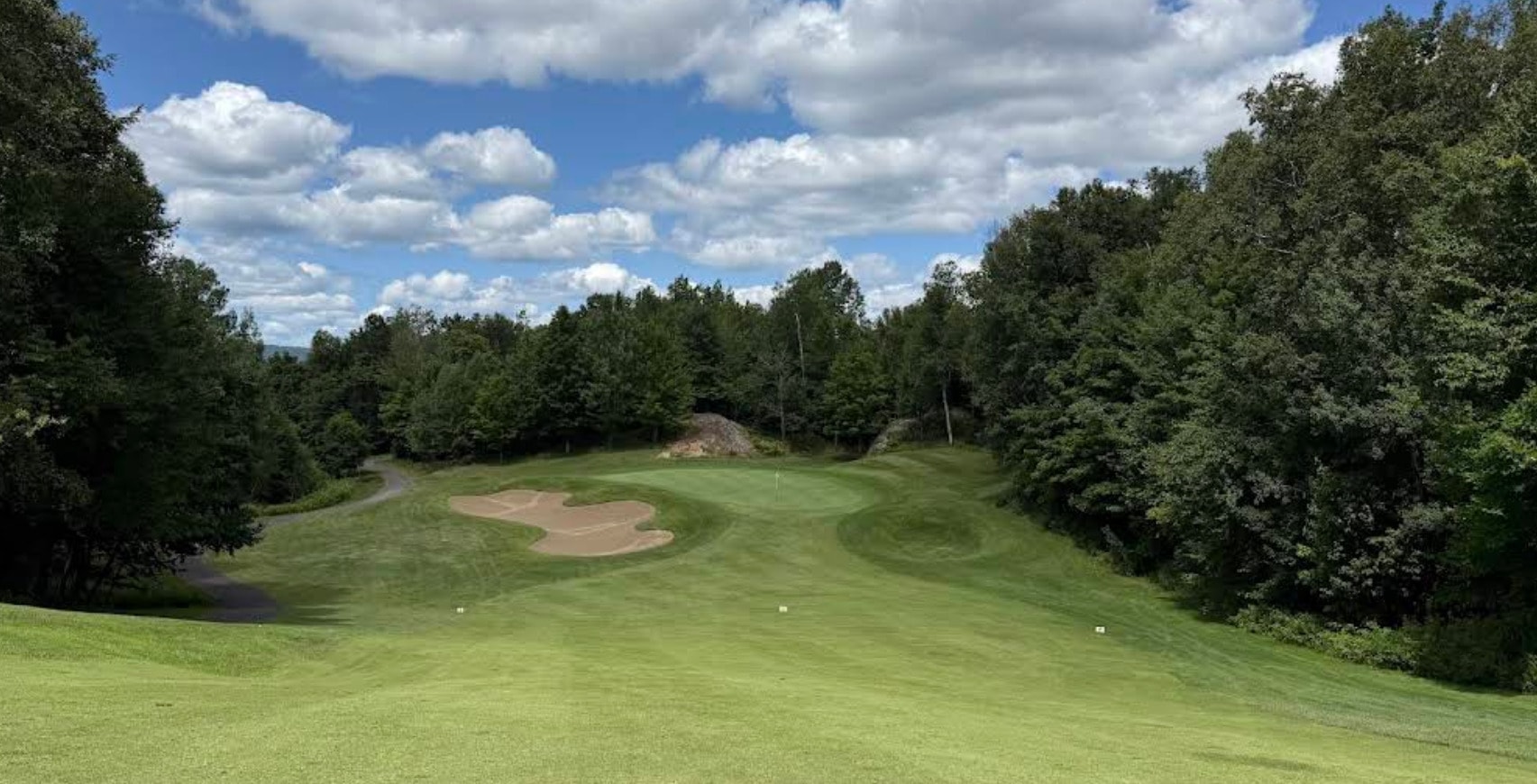 A view of Le Géant Golf Course at Mont-Tremblant, showcasing its lush fairways, elevated greens, and forested mountain backdrop under a bright summer A view of Le Géant Golf Course at Mont-Tremblant, showcasing its lush fairways, elevated greens, and forested mountain backdrop under a bright summer