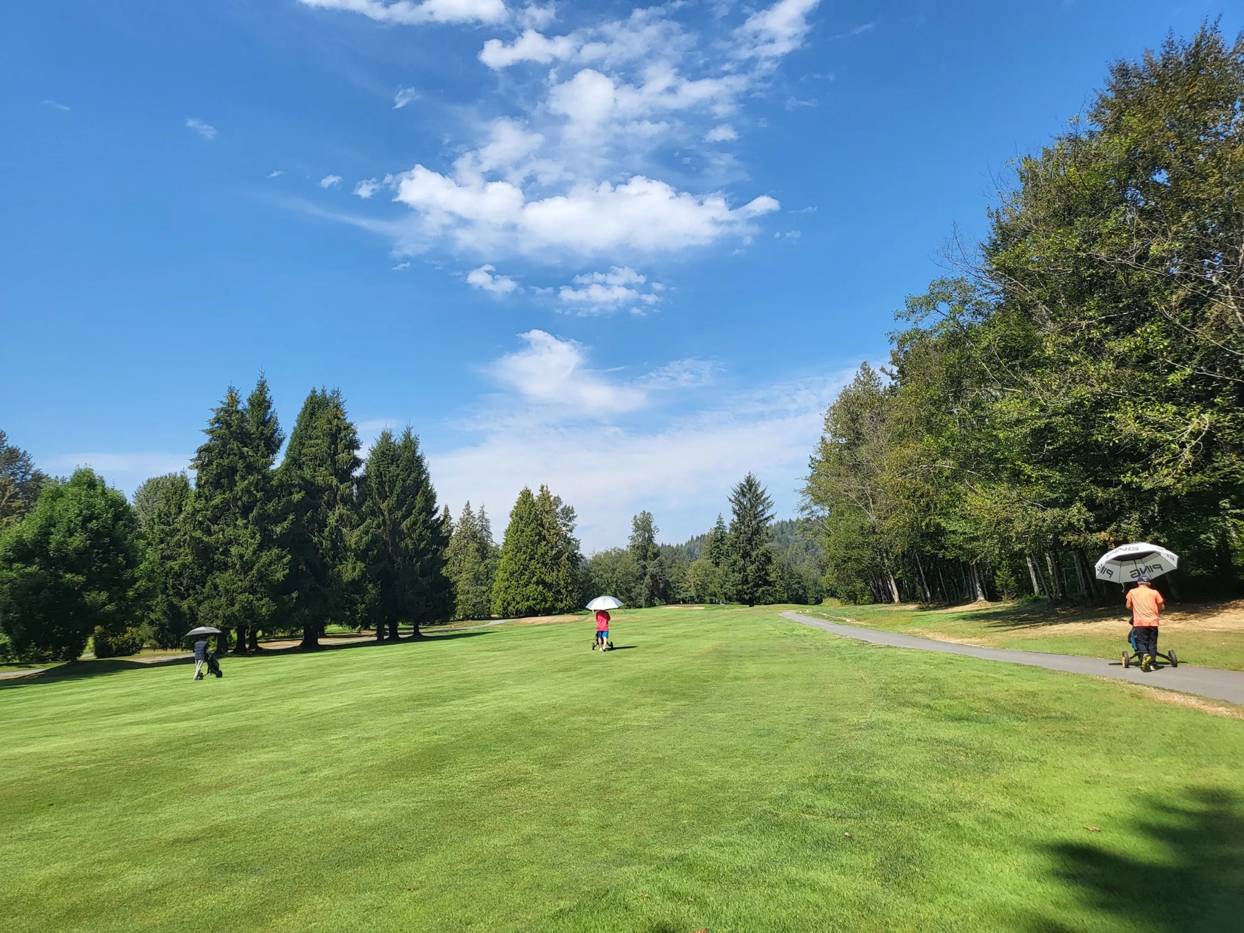 Golfers stroll the fairway under umbrellas on a sunny day — wide open space and peaceful forest edges make Burnaby Mountain a scenic walk. Golfers stroll the fairway under umbrellas on a sunny day — wide open space and peaceful forest edges make Burnaby Mountain a scenic walk.