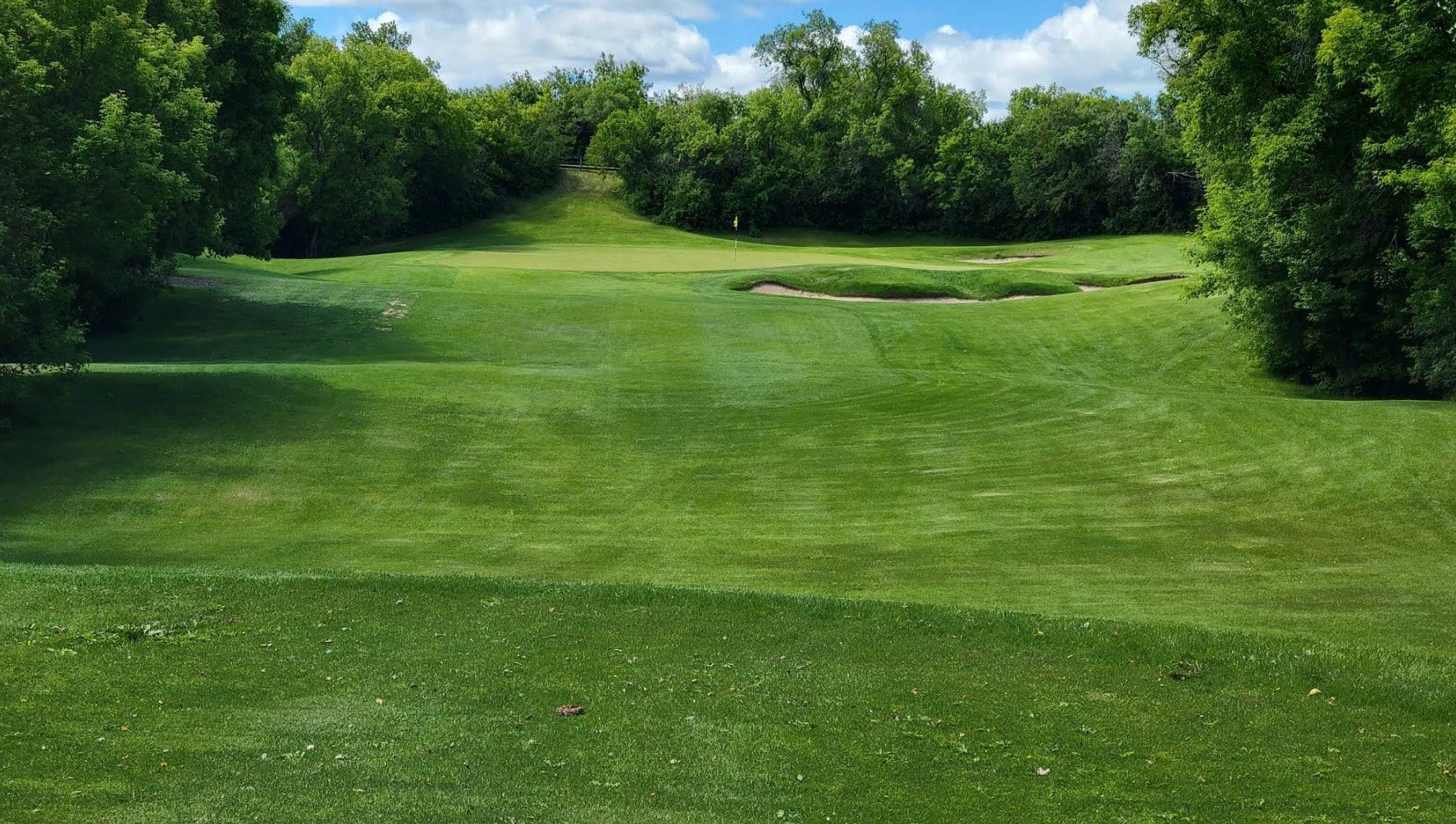 Lush tree-lined fairway leading up to a raised green at Holiday Park Golf Course in Saskatoon. Lush tree-lined fairway leading up to a raised green at Holiday Park Golf Course in Saskatoon.