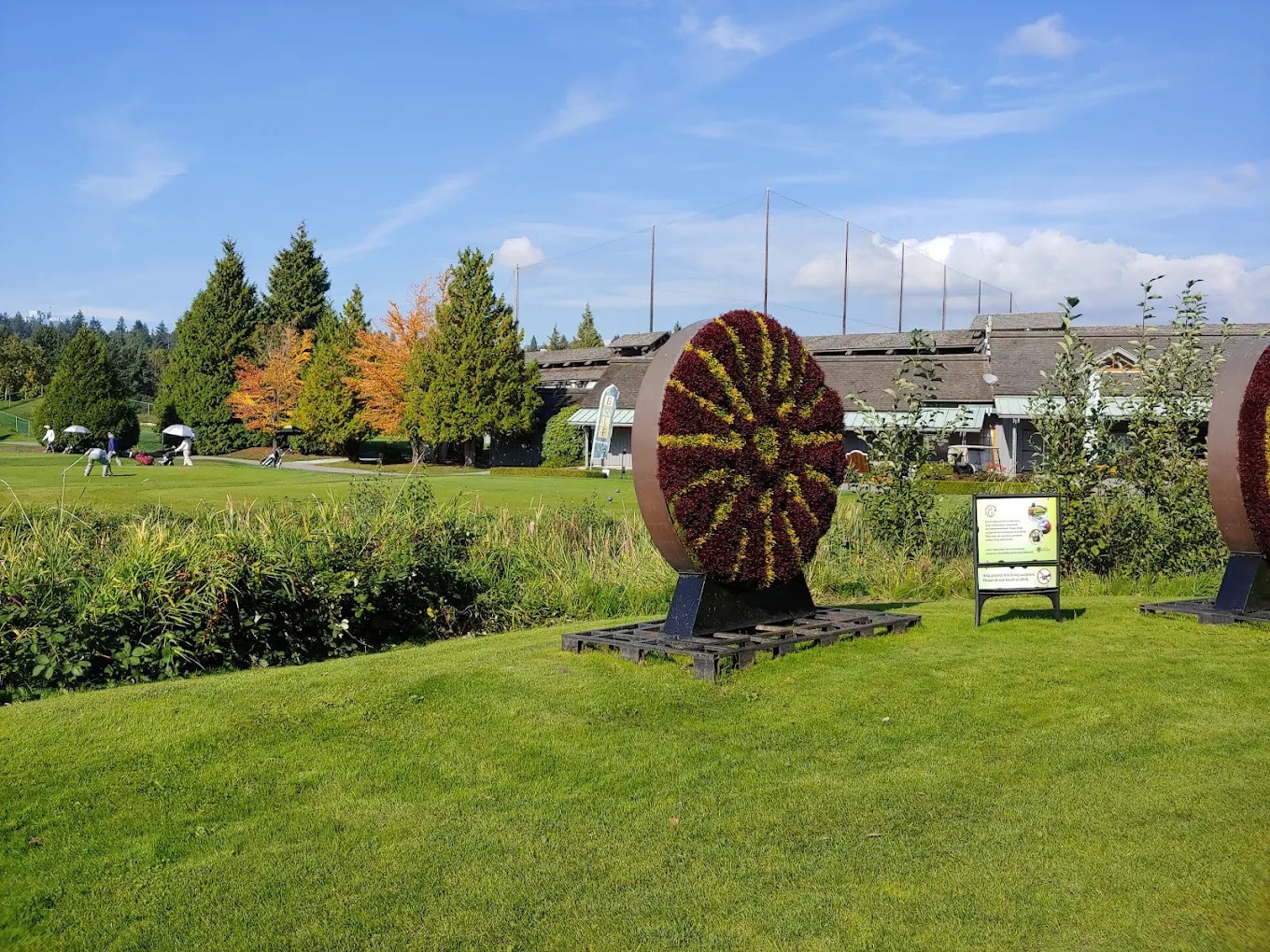 Riverway’s front entrance features floral wheel sculptures and fall colors, with golfers warming up near the clubhouse and driving range Riverway’s front entrance features floral wheel sculptures and fall colors, with golfers warming up near the clubhouse and driving range